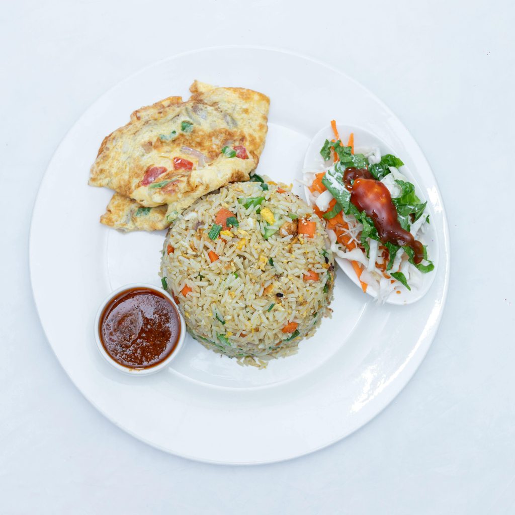 Tasty Ghanaian fried rice served with omelette, salad, and spicy sauce.